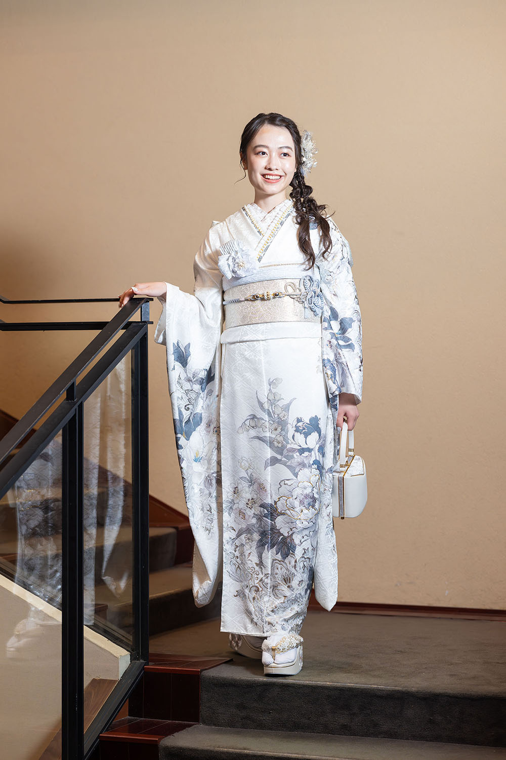 白地に青い花柄の振袖を着て階段に立つ女性