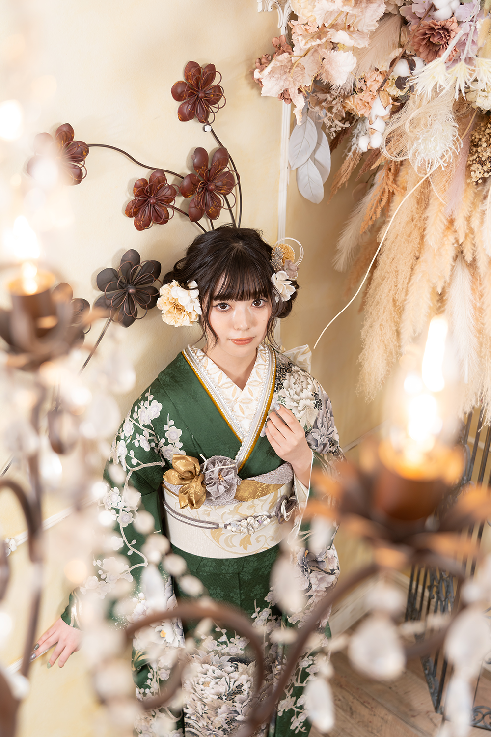 薄めの緑振袖にベージュの帯を身に纏った女性が、ドライフラワーに囲まれたスタジオで撮影をしている